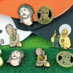 Collection of custom enamel pins featuring cultural portraits, saints, and warriors displayed on hats