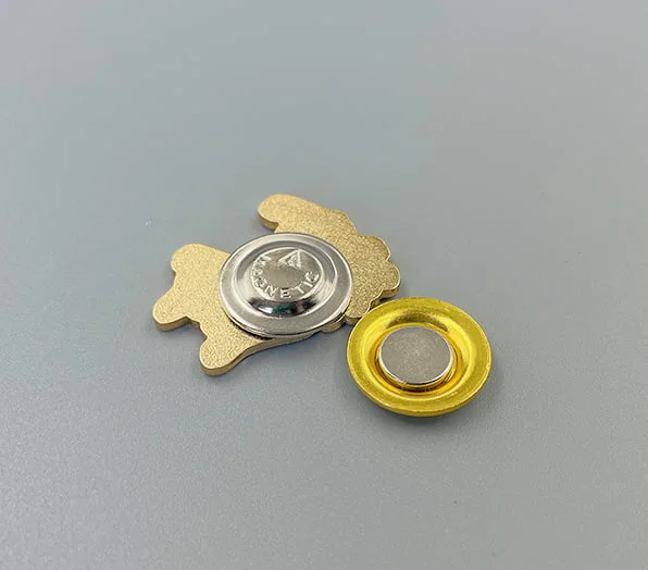 A custom gold-toned pin backing featuring a round magnetic attachment with a central magnet button and a matching gold-trimmed magnetic base.