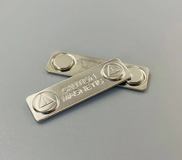 Two metal bar magnets designed for pin backings, featuring circular magnetic buttons