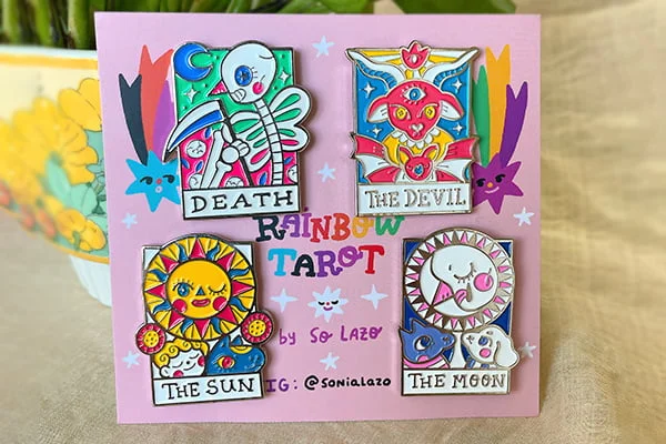 Set of four "Rainbow Tarot" hard enamel pins designed by So Lazo, featuring Death, The Devil, The Sun, and The Moon displayed on a pink backing card.