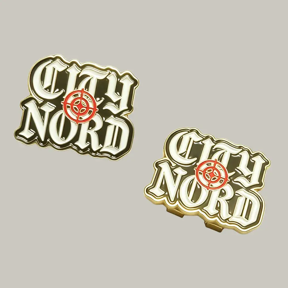 A pair of custom gold metal enamel accessories featuring the "City Nord" logo with a red crosshair symbol, shown as a hat pin next to a heavy-duty hat clip back attachment.