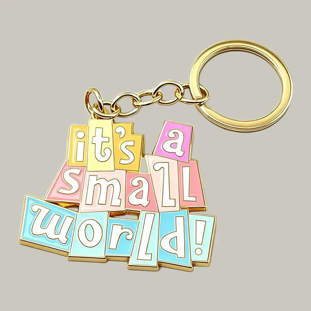 A custom gold enamel keychain with "it's a small world!" written in colorful block lettering, attached to a shiny gold metal chain and key ring.