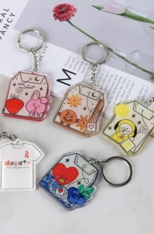 Collection of custom acrylic keychains featuring cute cartoon character tea bag designs with fruits and a white t-shirt shaped keychain with text.