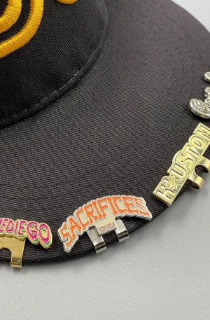 Custom Enamel Hat Clip - Assorted "Slimediego," "Sacrifices," "Houston," and Cursive Script Magnetic Hat Clips Attached to the Brim of a Black Baseball Cap