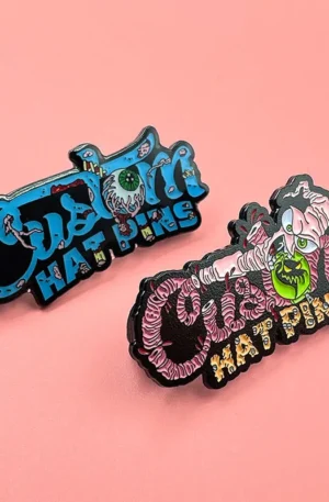 Custom Horror-Themed Eyeball and Mummy Style Enamel Hat Pins with Blue and Pink Lettering Displayed on a Pink Background