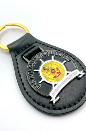 Custom black leather keychain featuring a teardrop design, a gold keyring, and an embedded metal ship wheel badge with custom engraved organization branding.