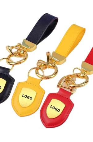 Custom leather keychain set featuring black, yellow, and red shield-shaped designs with embedded gold "LOGO" metal badges, matching wrist straps, and gold hardware.