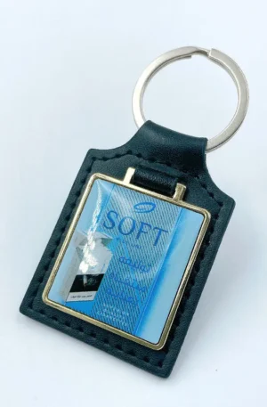 Custom black leather keychain featuring a rectangular design with fine perimeter stitching, a silver split keyring, and an embedded metal badge displaying a blue "SOFT" brand emblem.