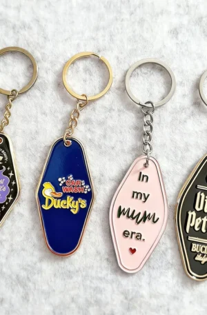 Collection of custom retro motel style metal keychains featuring colorful enamel designs, unique typography, and keyring attachments.