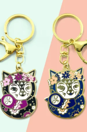 Pair of custom gold metal keychains featuring cute owl enamel charms with floral wreaths in contrasting black and blue colorways with gold lobster clasp keyrings.