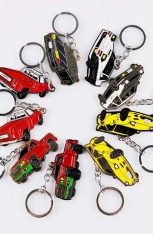 Assorted collection of custom car-shaped metal keychains featuring various vehicle designs like red pickup trucks, yellow sports cars, and police cars with enamel details and keyrings.