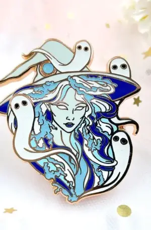 Custom enamel pin featuring a witch with hat surrounded by cute ghosts, blue glitter details and gold plating