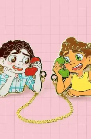 Custom enamel pin set featuring two animated boys from Luca connected by a gold chain talking on telephones with heart details