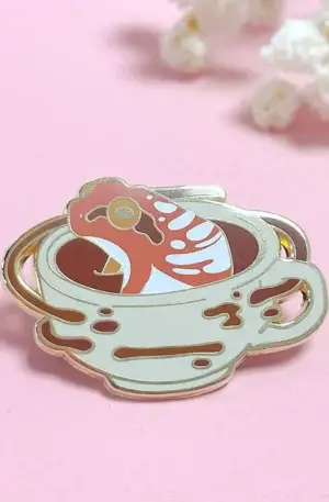 Custom enamel pin featuring a cute red and white frog relaxing in a coffee cup with splatter details and gold plating