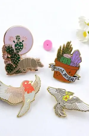 Custom enamel pin set featuring botanical and animal designs including an armadillo with cacti, a Plant Magic potted succulent, and flying birds with gold plating