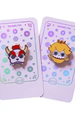 Custom enamel pin set featuring gaming-inspired skull character designs including Bowser and Princess Peach on holographic backing cards with gold plating
