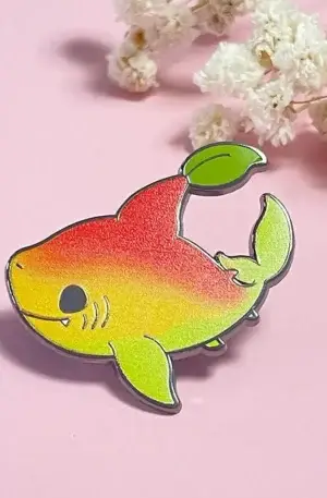 Custom enamel pin featuring a cute mango-themed shark with a yellow, red, and green gradient body, leaf fin, and metallic trim