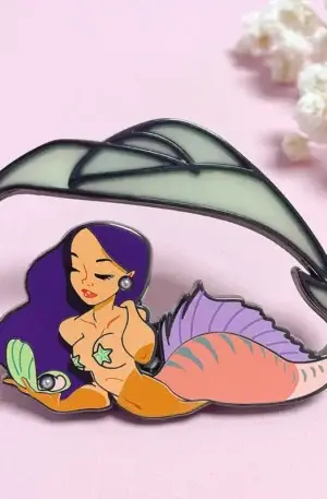Custom enamel pin featuring a beautiful mermaid with purple hair, a pink fish tail, holding a shell with a pearl, under a glowing wave or fin with gold plating