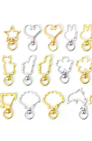 An assortment of fancy shaped metal snap hooks and split-keyrings in gold and silver finishes, featuring creative designs like stars, hearts, cats, rabbits, flowers, moons, and dolphins for custom keychains and bag charms.