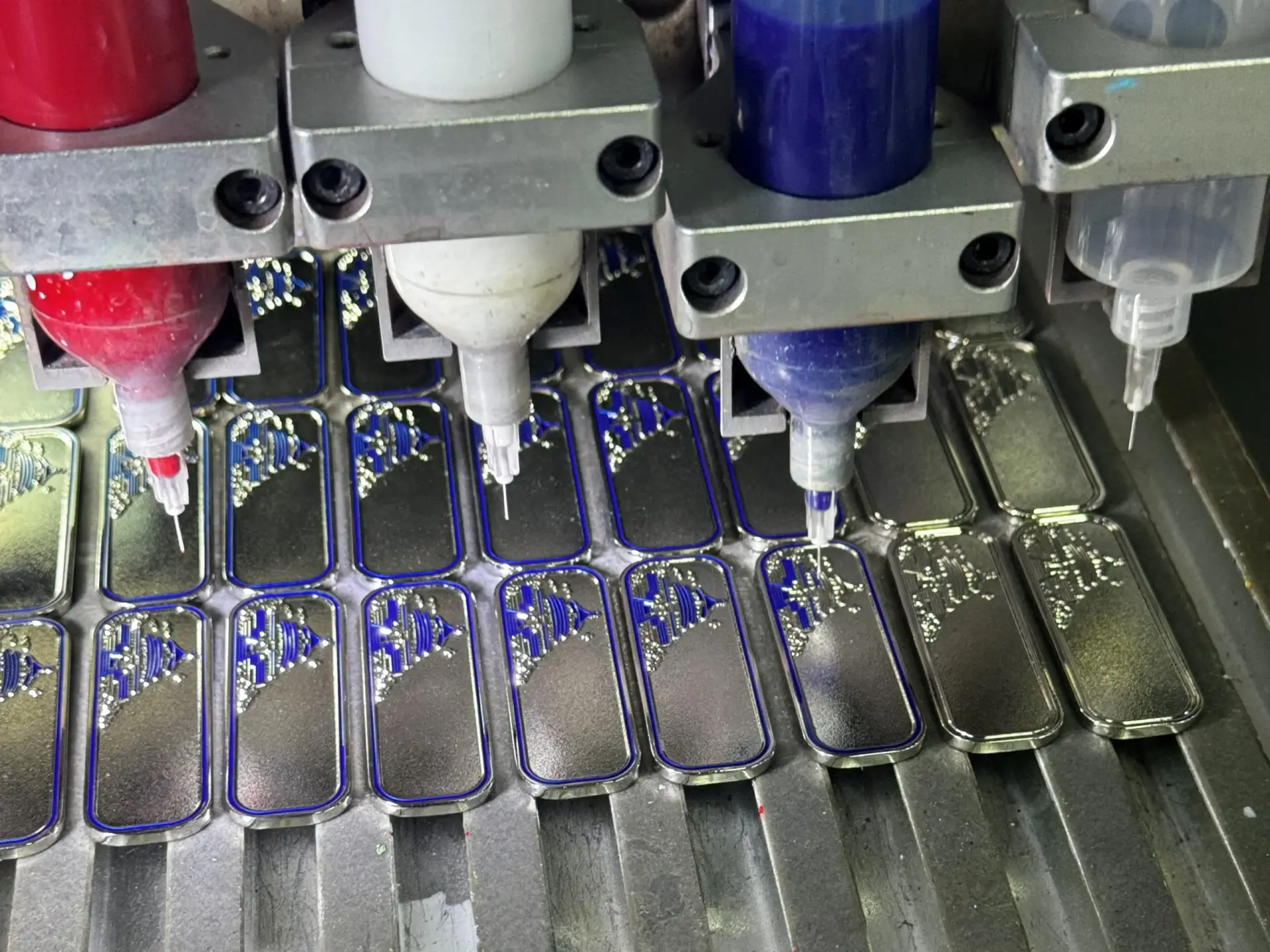 Automatic enamel dispensing machine precisely filling colored liquid into custom metal pin recesses.