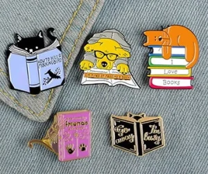 Custom bookish enamel pins featuring reading cats and dogs displayed on denim jacket