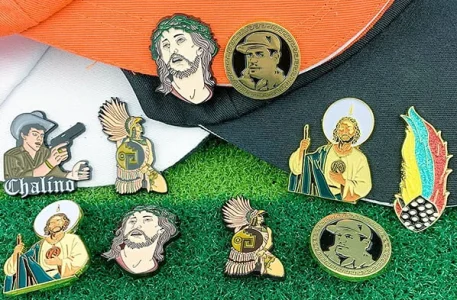 Collection of custom enamel pins featuring cultural portraits, saints, and warriors displayed on hats
